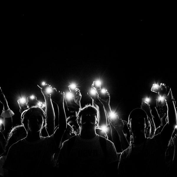 Silhouettes of people holding up phones with flashlights on.